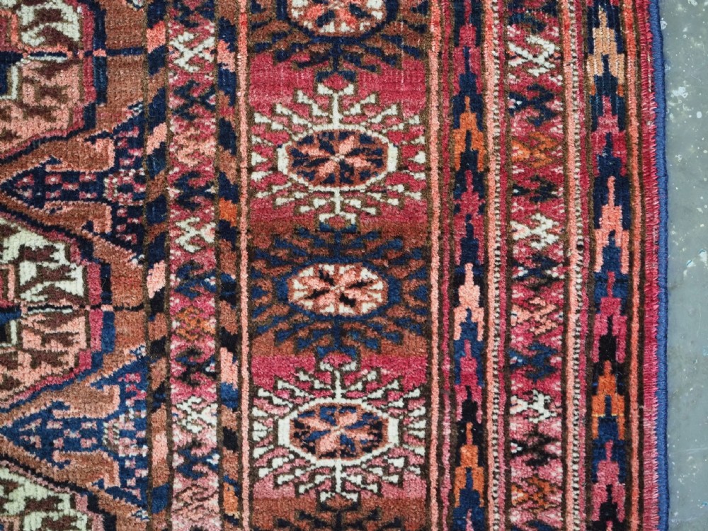 An antique rectangular hand-knotted wool Tekke Turkmen rug featuring repeating octagonal gul motifs in terracotta, navy, and cream tones with geometric borders. View IX