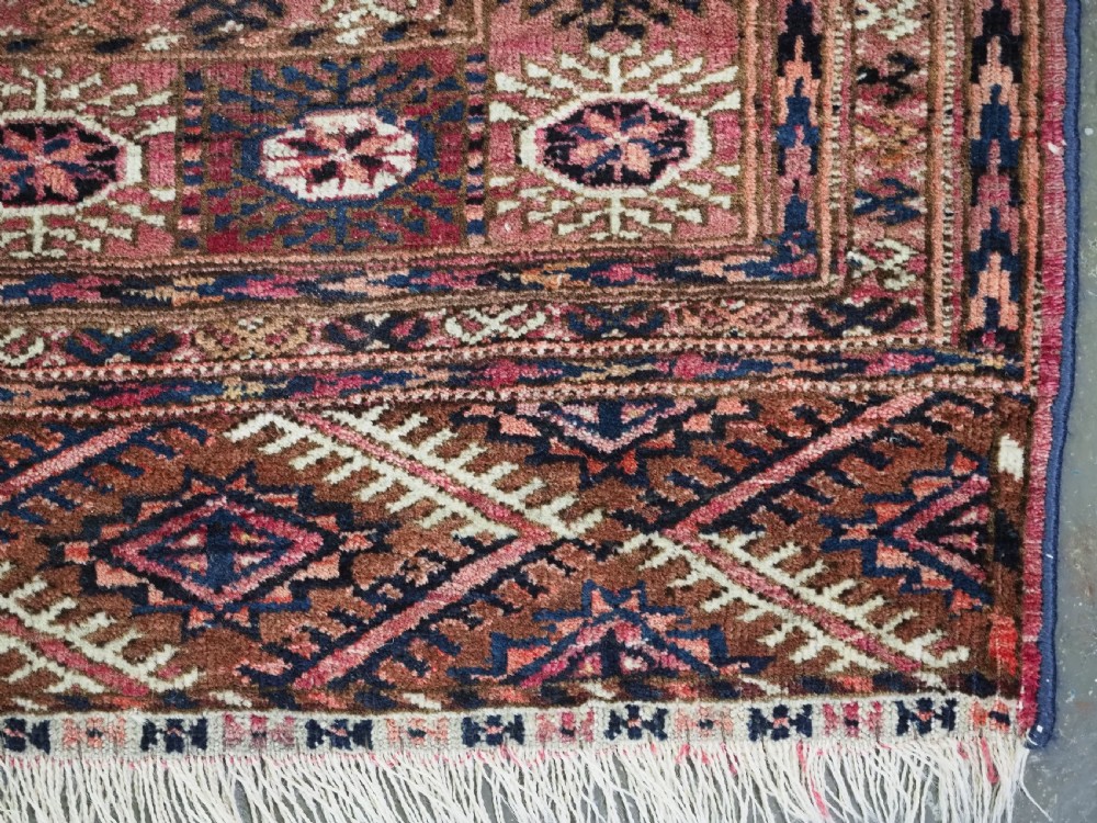 An antique rectangular hand-knotted wool Tekke Turkmen rug featuring repeating octagonal gul motifs in terracotta, navy, and cream tones with geometric borders. View X
