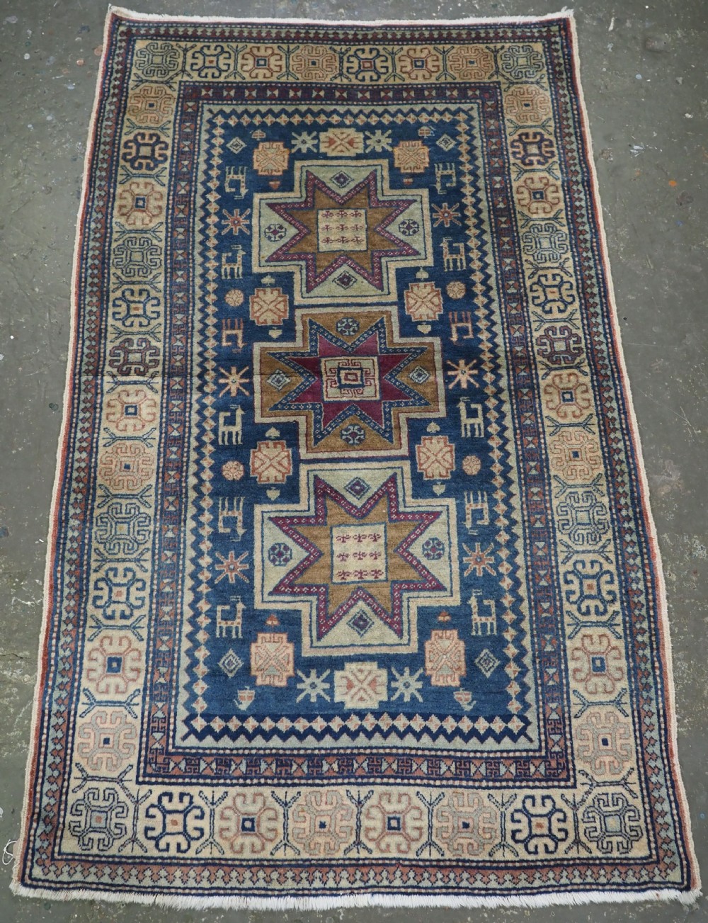An antique Caucasian hand-knotted wool rug featuring three star medallions on a navy blue field with geometric borders.