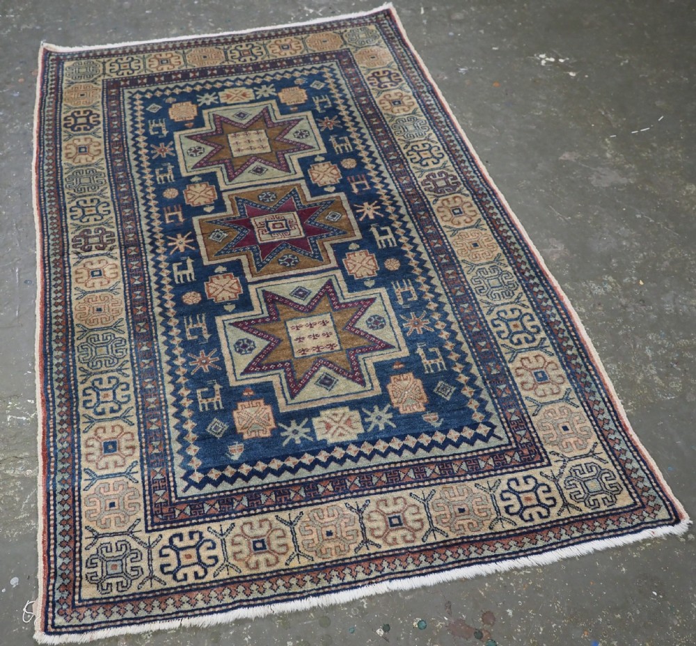 An antique Caucasian hand-knotted wool rug featuring three star medallions on a navy blue field with geometric borders. View II