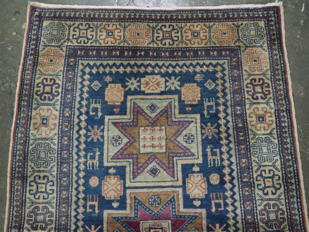 An antique Caucasian hand-knotted wool rug featuring three star medallions on a navy blue field with geometric borders. View III