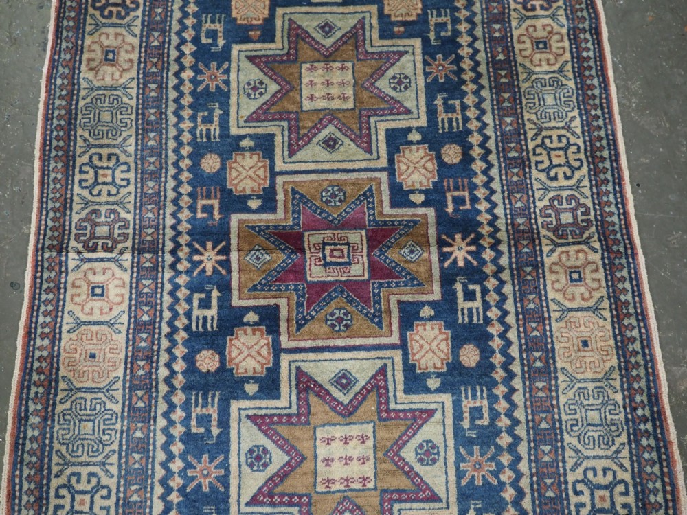 An antique Caucasian hand-knotted wool rug featuring three star medallions on a navy blue field with geometric borders. View IV