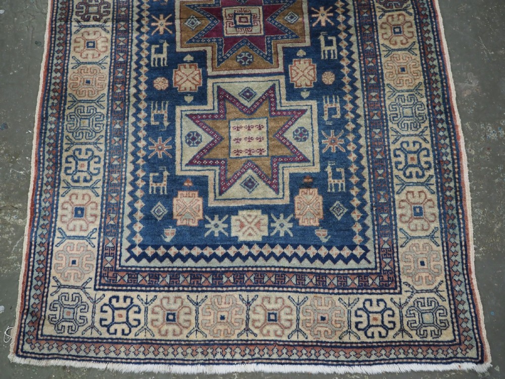 An antique Caucasian hand-knotted wool rug featuring three star medallions on a navy blue field with geometric borders. View V