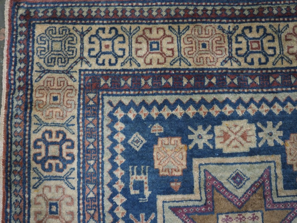 An antique Caucasian hand-knotted wool rug featuring three star medallions on a navy blue field with geometric borders. View VI