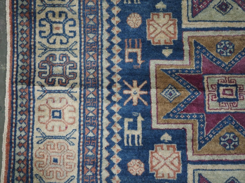 An antique Caucasian hand-knotted wool rug featuring three star medallions on a navy blue field with geometric borders. View VII