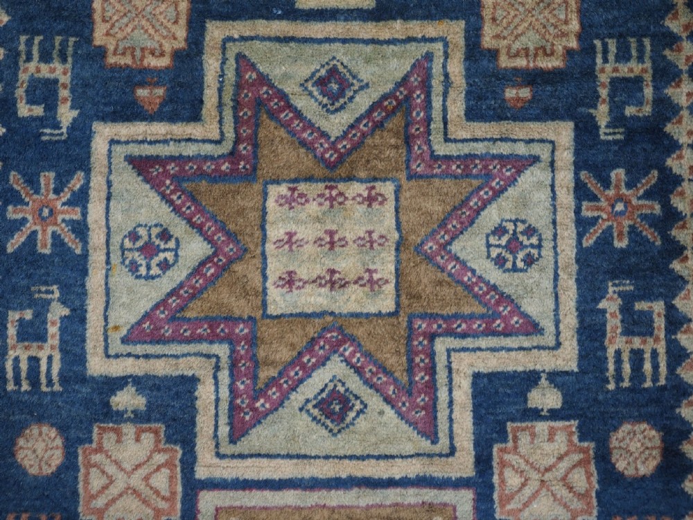 An antique Caucasian hand-knotted wool rug featuring three star medallions on a navy blue field with geometric borders. View VIII