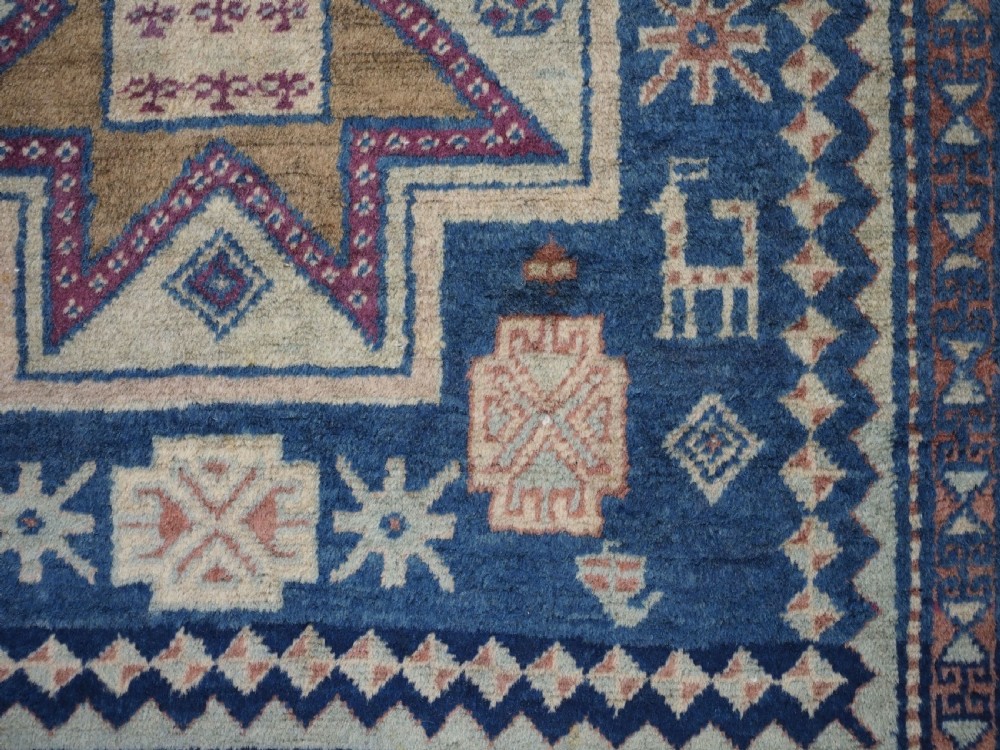 An antique Caucasian hand-knotted wool rug featuring three star medallions on a navy blue field with geometric borders. View X
