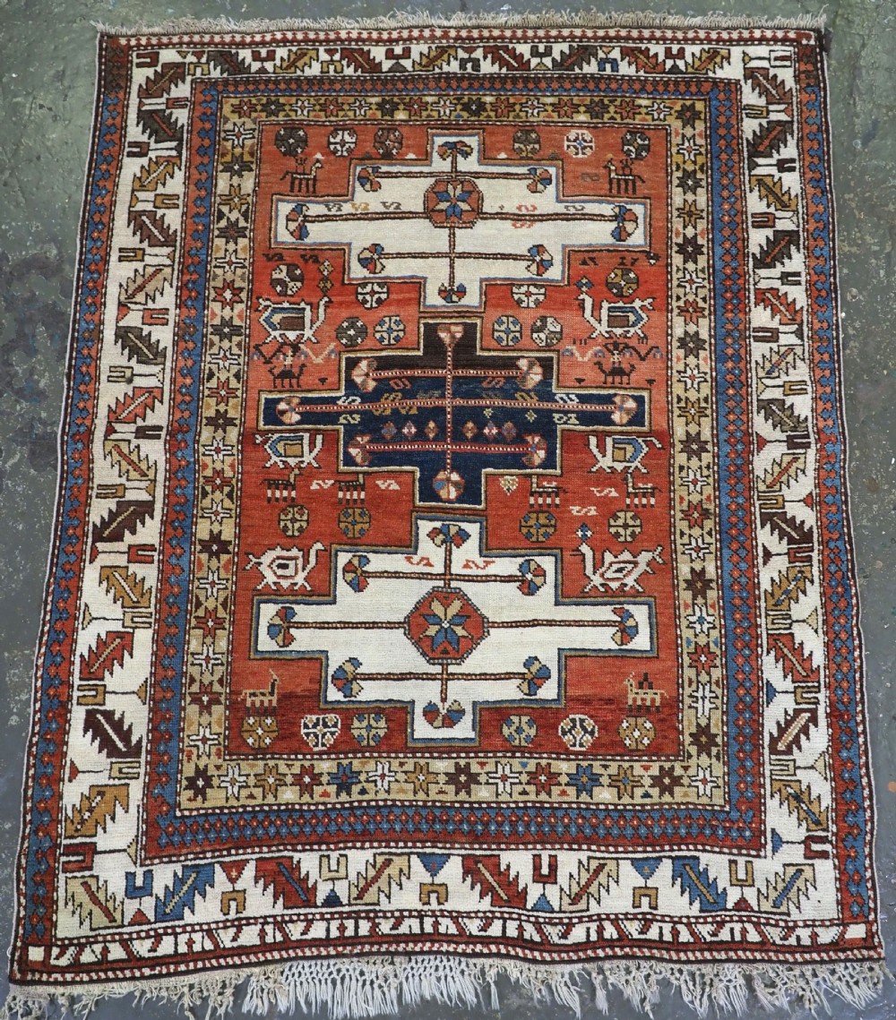 An antique hand-knotted Caucasian Shirvan wool rug with geometric central medallions, zoomorphic figures, and tribal borders in terracotta, cream, and navy blue.
