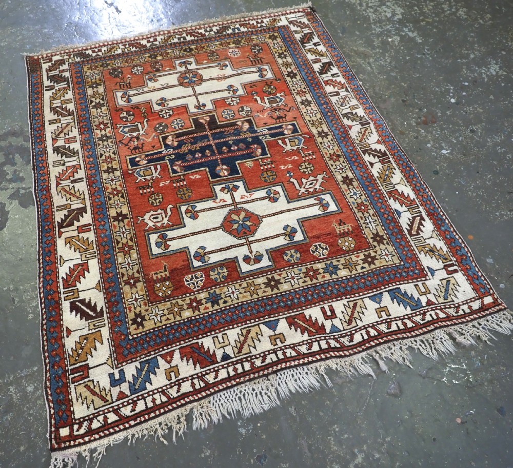 An antique hand-knotted Caucasian Shirvan wool rug with geometric central medallions, zoomorphic figures, and tribal borders in terracotta, cream, and navy blue. View II