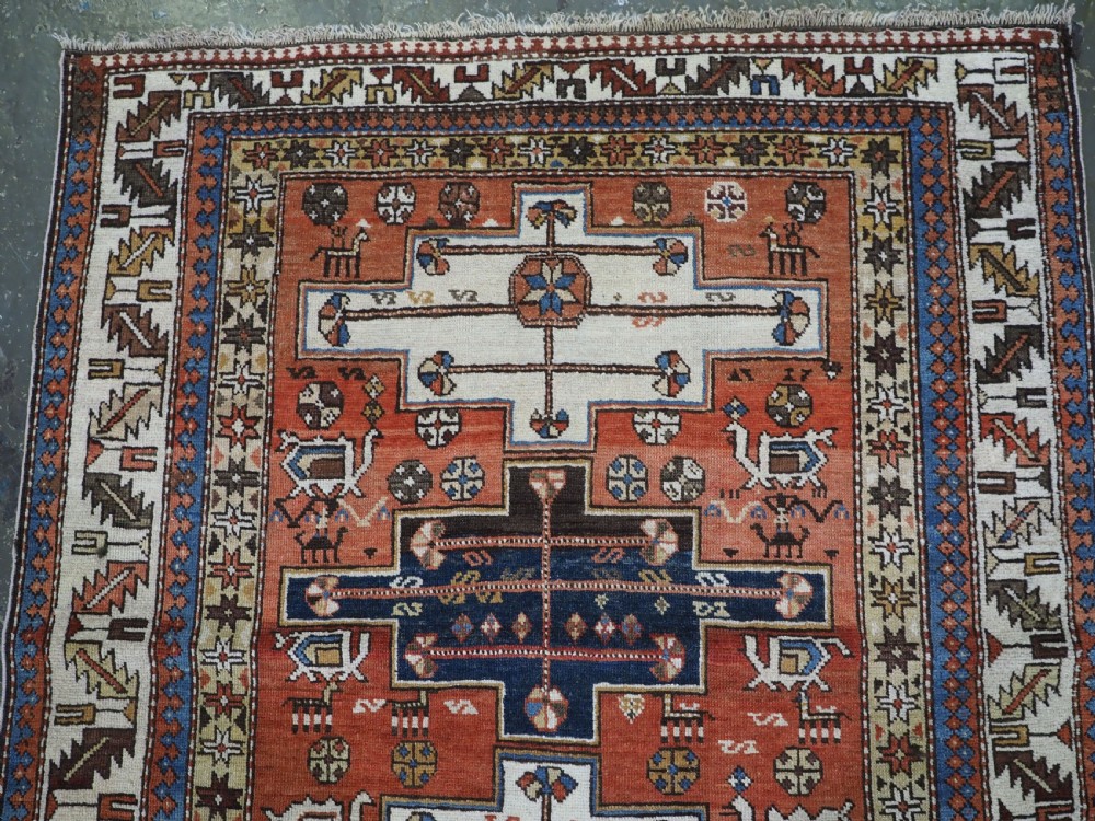 An antique hand-knotted Caucasian Shirvan wool rug with geometric central medallions, zoomorphic figures, and tribal borders in terracotta, cream, and navy blue. View III