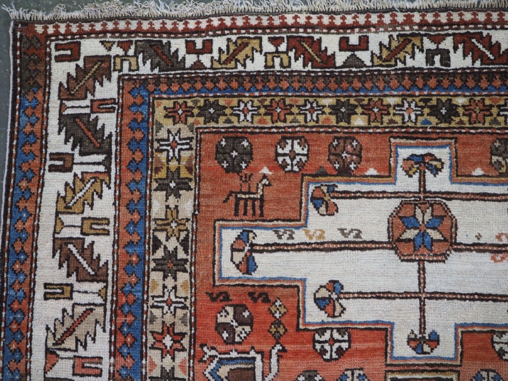 An antique hand-knotted Caucasian Shirvan wool rug with geometric central medallions, zoomorphic figures, and tribal borders in terracotta, cream, and navy blue. View IV