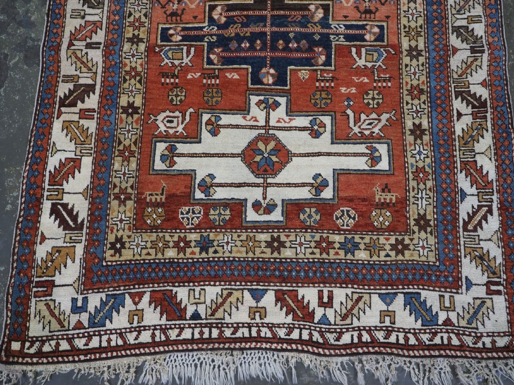 An antique hand-knotted Caucasian Shirvan wool rug with geometric central medallions, zoomorphic figures, and tribal borders in terracotta, cream, and navy blue. View V