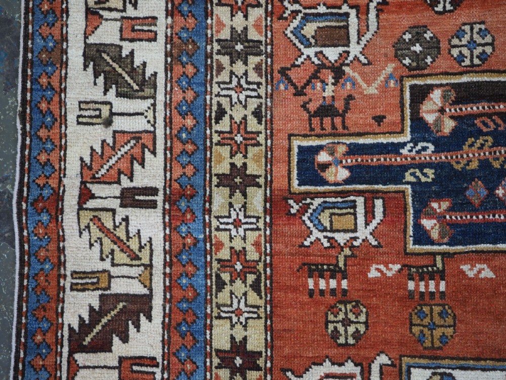 An antique hand-knotted Caucasian Shirvan wool rug with geometric central medallions, zoomorphic figures, and tribal borders in terracotta, cream, and navy blue. View VI