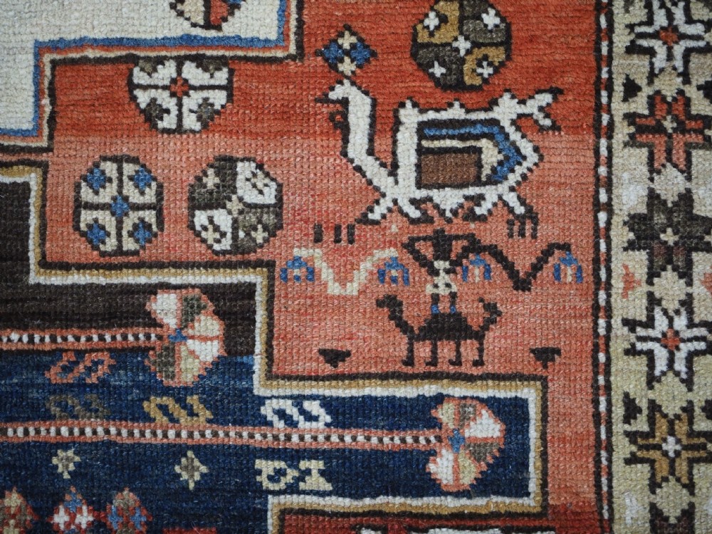 An antique hand-knotted Caucasian Shirvan wool rug with geometric central medallions, zoomorphic figures, and tribal borders in terracotta, cream, and navy blue. View IX