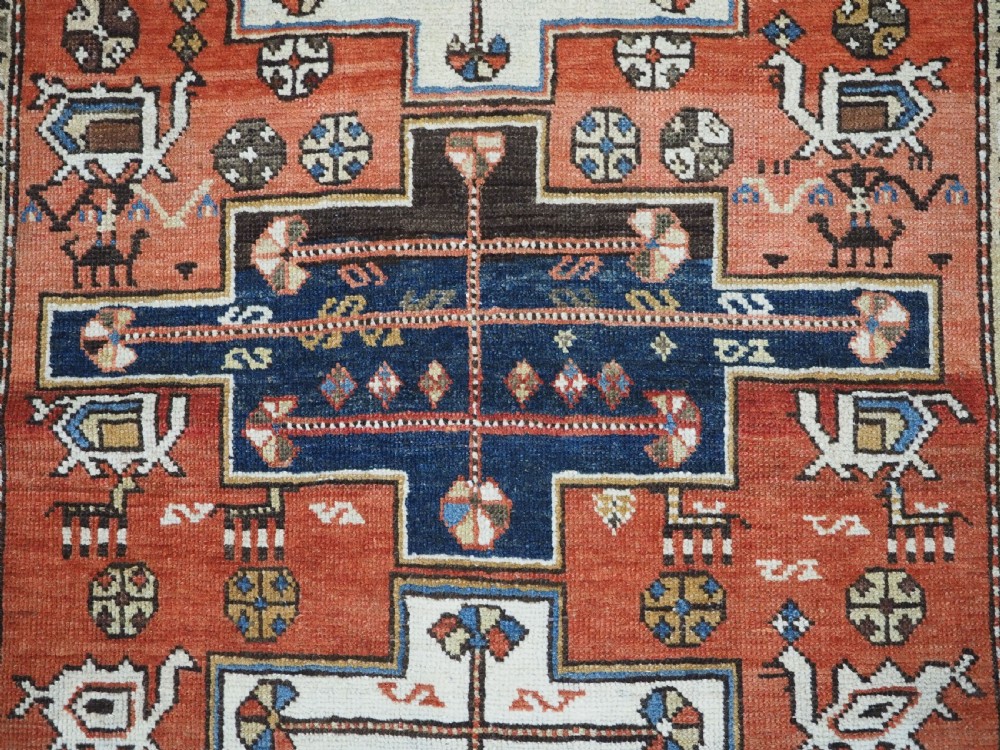An antique hand-knotted Caucasian Shirvan wool rug with geometric central medallions, zoomorphic figures, and tribal borders in terracotta, cream, and navy blue. View X