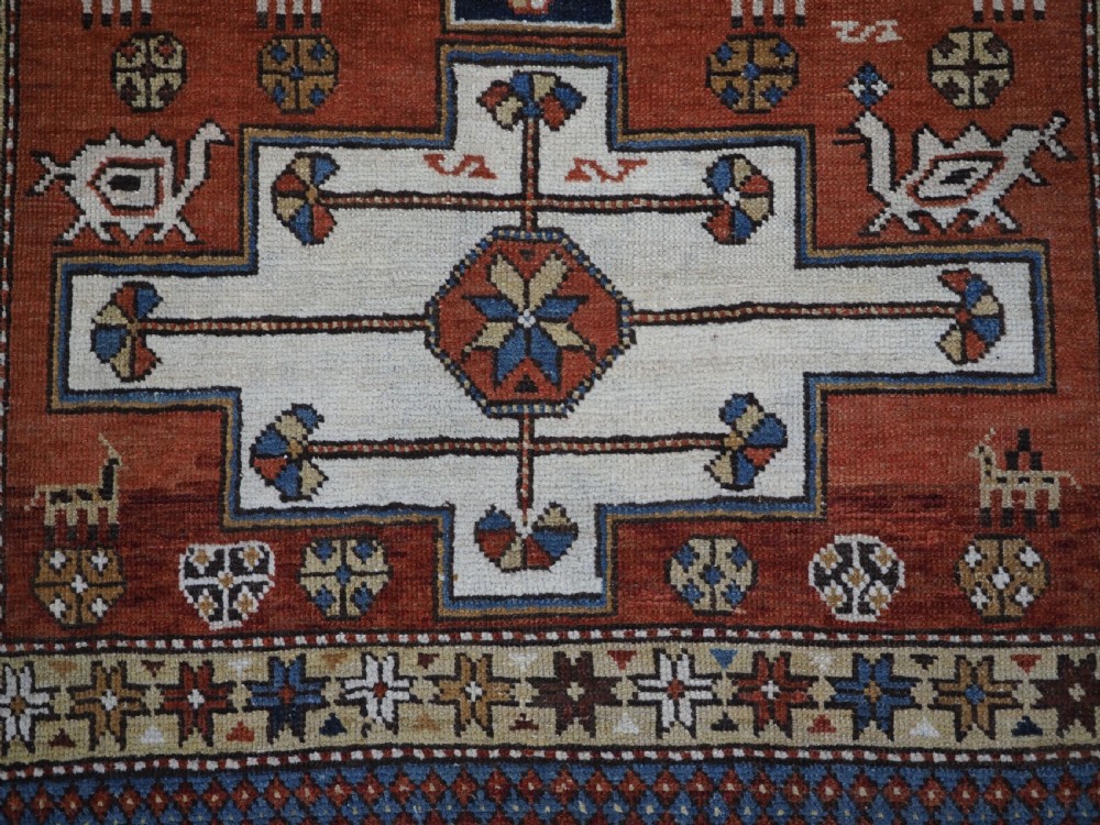 An antique hand-knotted Caucasian Shirvan wool rug with geometric central medallions, zoomorphic figures, and tribal borders in terracotta, cream, and navy blue. View XI