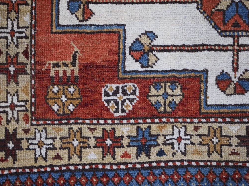 An antique hand-knotted Caucasian Shirvan wool rug with geometric central medallions, zoomorphic figures, and tribal borders in terracotta, cream, and navy blue. View XII