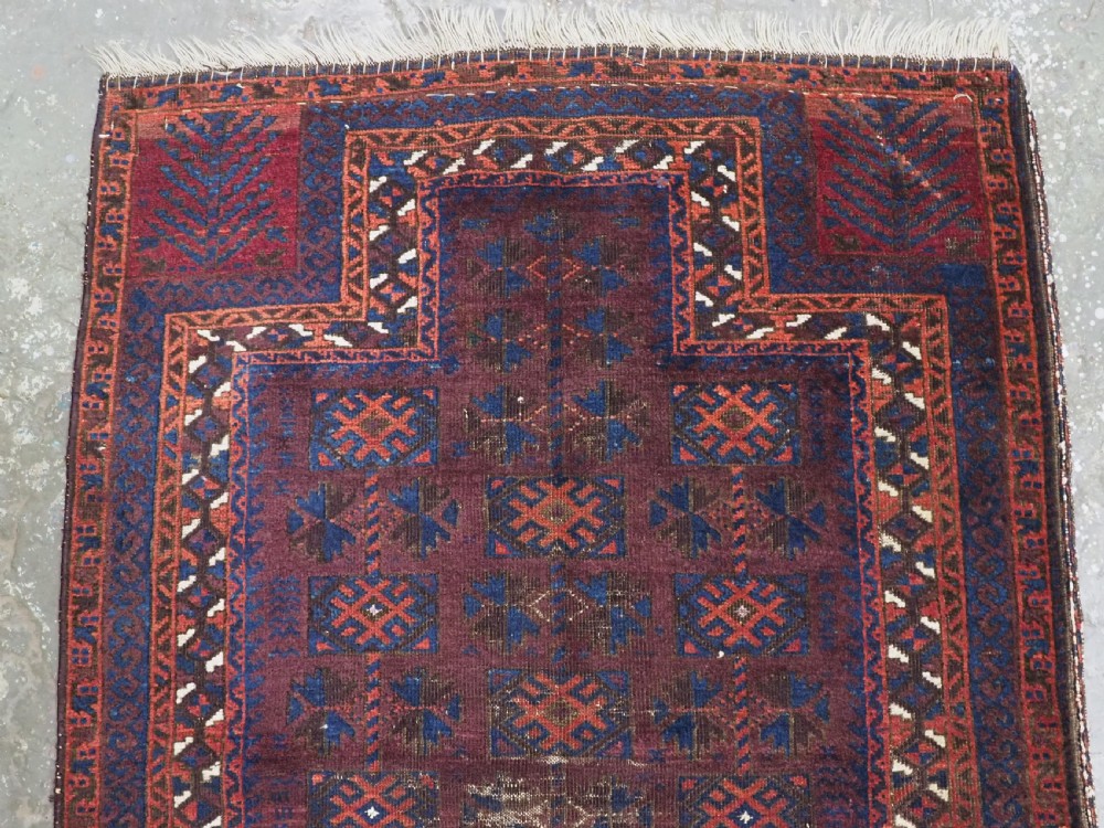 An antique hand-knotted wool prayer rug featuring a defined mihrab arch, geometric box patterns, and deep aubergine, rust red, and indigo blue tones. View III