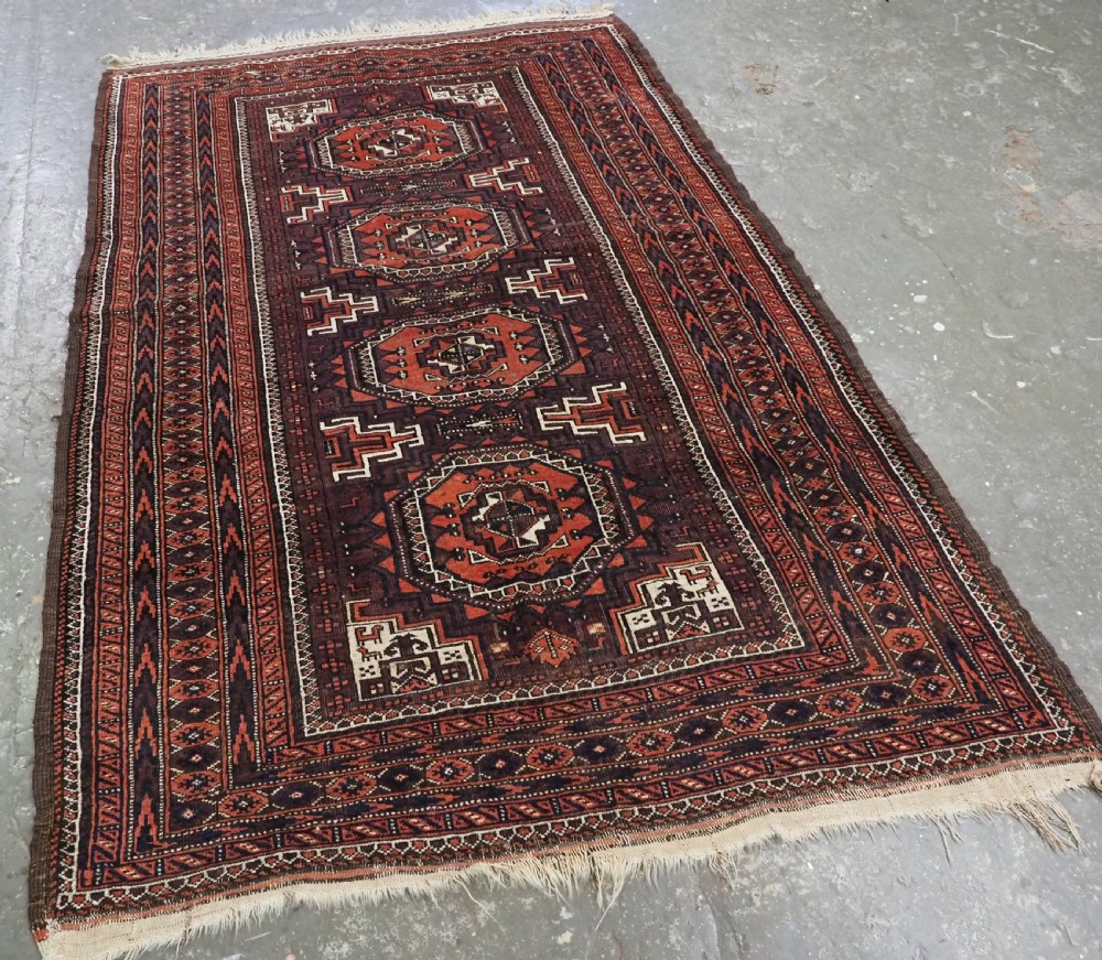 An antique hand-knotted wool Baluch rug featuring four octagonal central medallions on a deep aubergine ground with geometric borders. View II
