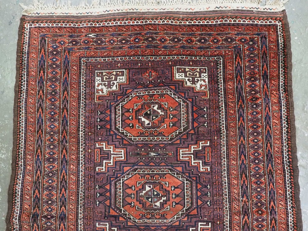 An antique hand-knotted wool Baluch rug featuring four octagonal central medallions on a deep aubergine ground with geometric borders. View III