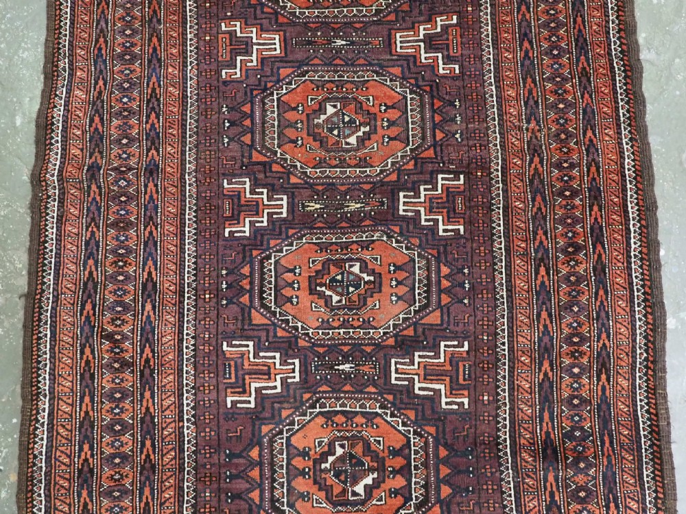 An antique hand-knotted wool Baluch rug featuring four octagonal central medallions on a deep aubergine ground with geometric borders. View IV