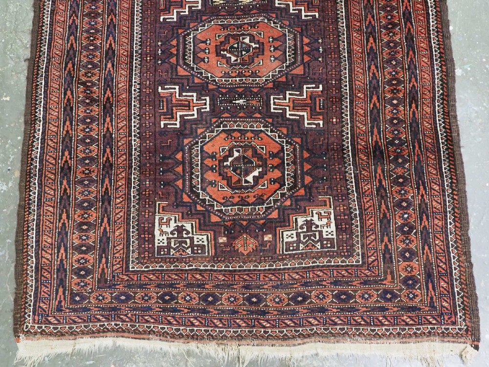 An antique hand-knotted wool Baluch rug featuring four octagonal central medallions on a deep aubergine ground with geometric borders. View V