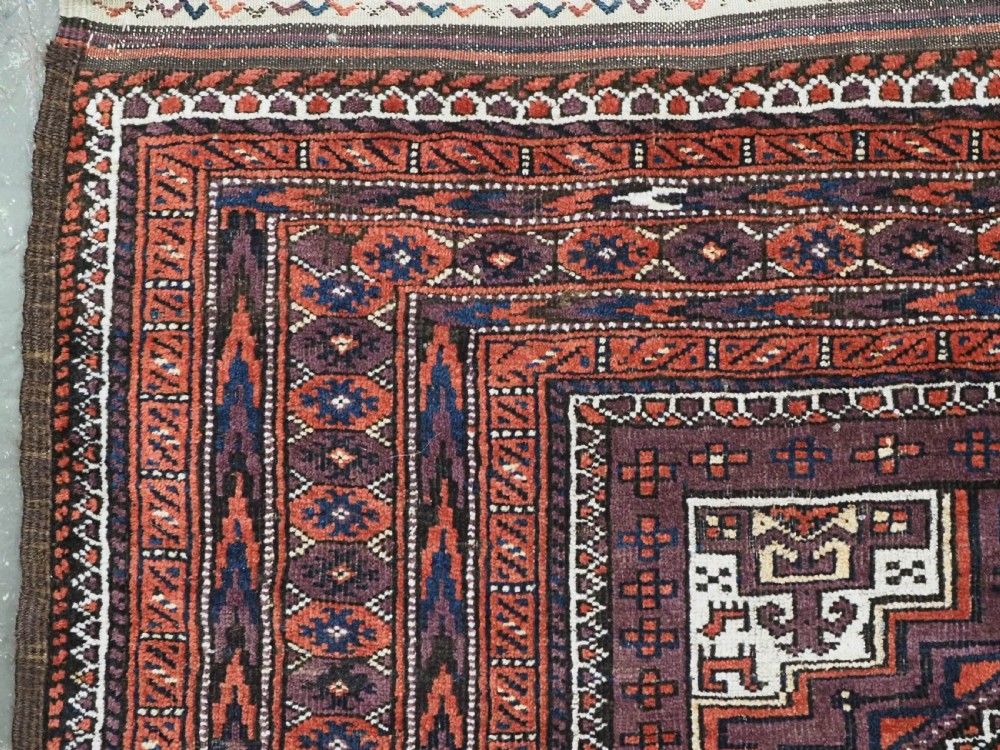 An antique hand-knotted wool Baluch rug featuring four octagonal central medallions on a deep aubergine ground with geometric borders. View VI