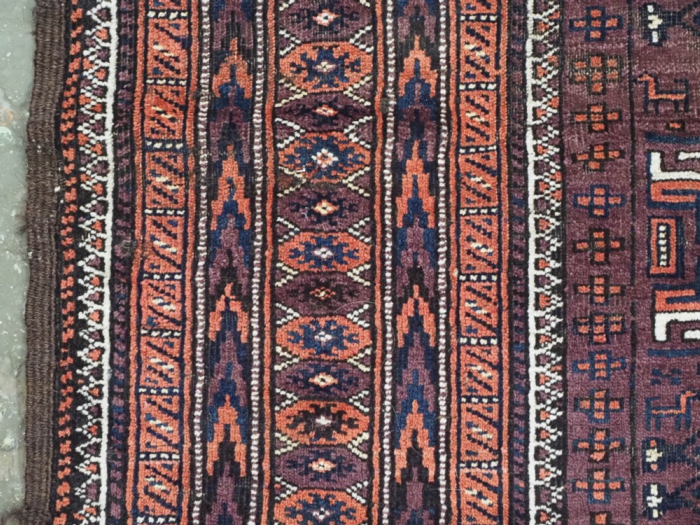An antique hand-knotted wool Baluch rug featuring four octagonal central medallions on a deep aubergine ground with geometric borders. View VII