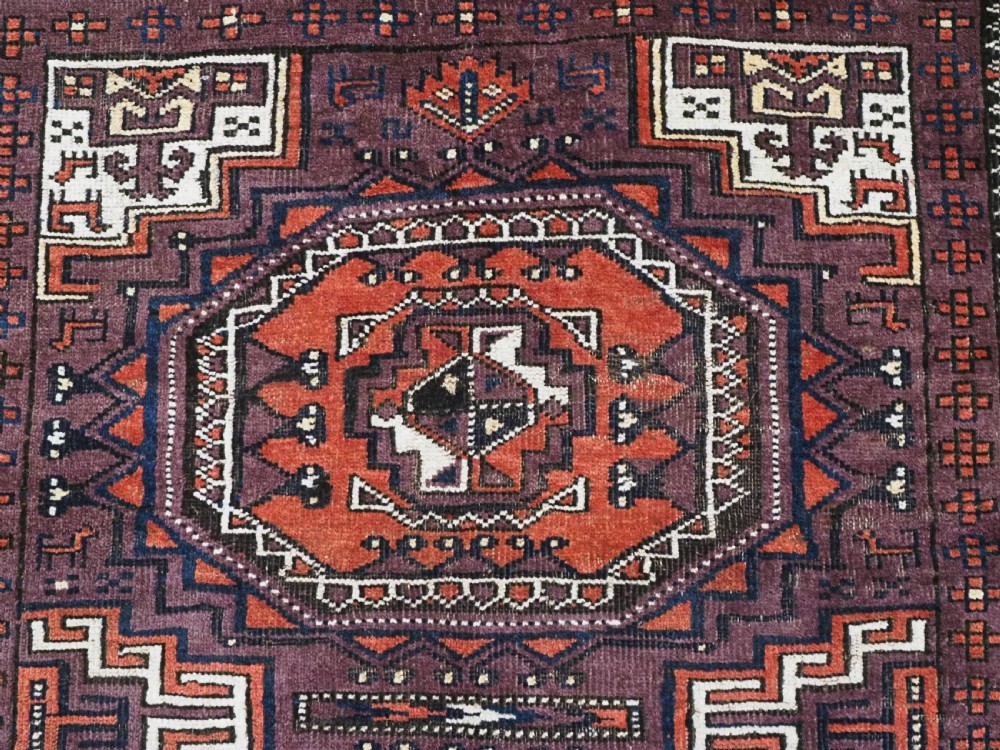An antique hand-knotted wool Baluch rug featuring four octagonal central medallions on a deep aubergine ground with geometric borders. View VIII