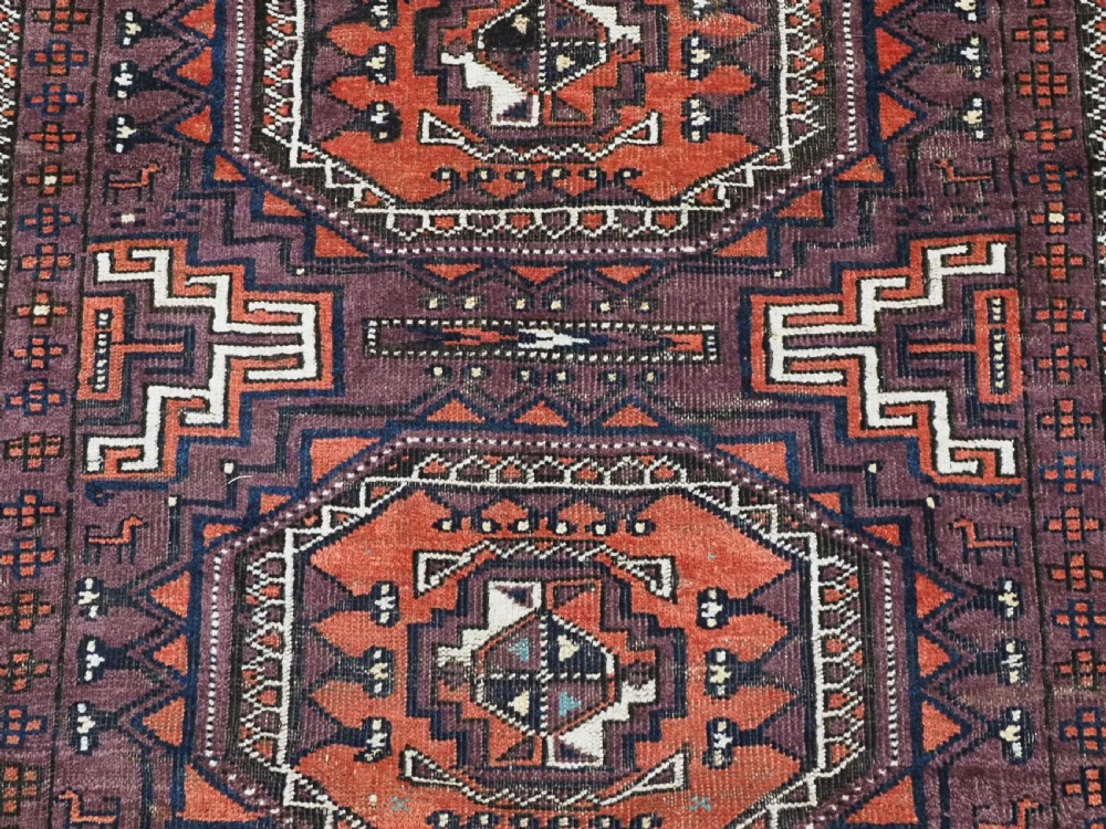 An antique hand-knotted wool Baluch rug featuring four octagonal central medallions on a deep aubergine ground with geometric borders. View IX