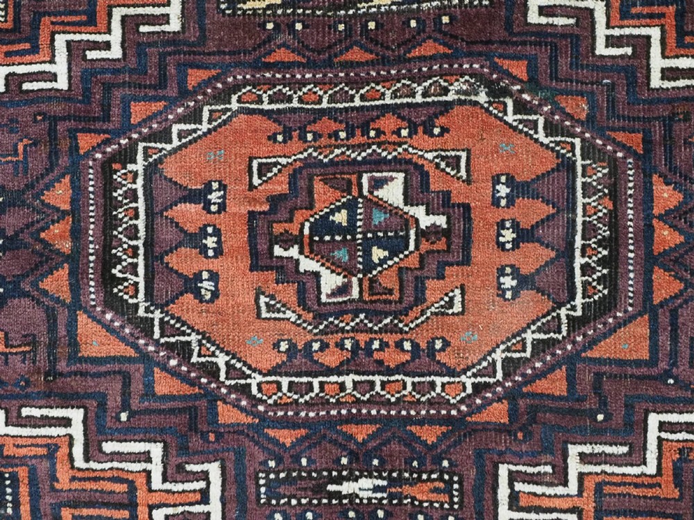 An antique hand-knotted wool Baluch rug featuring four octagonal central medallions on a deep aubergine ground with geometric borders. View X