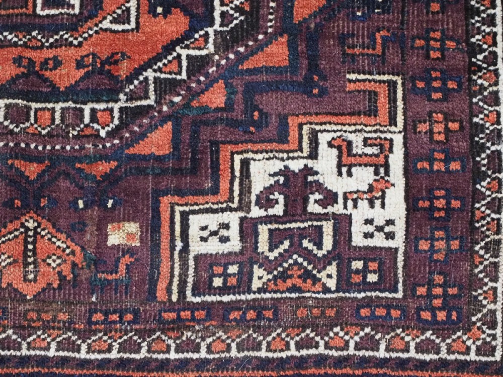 An antique hand-knotted wool Baluch rug featuring four octagonal central medallions on a deep aubergine ground with geometric borders. View XII
