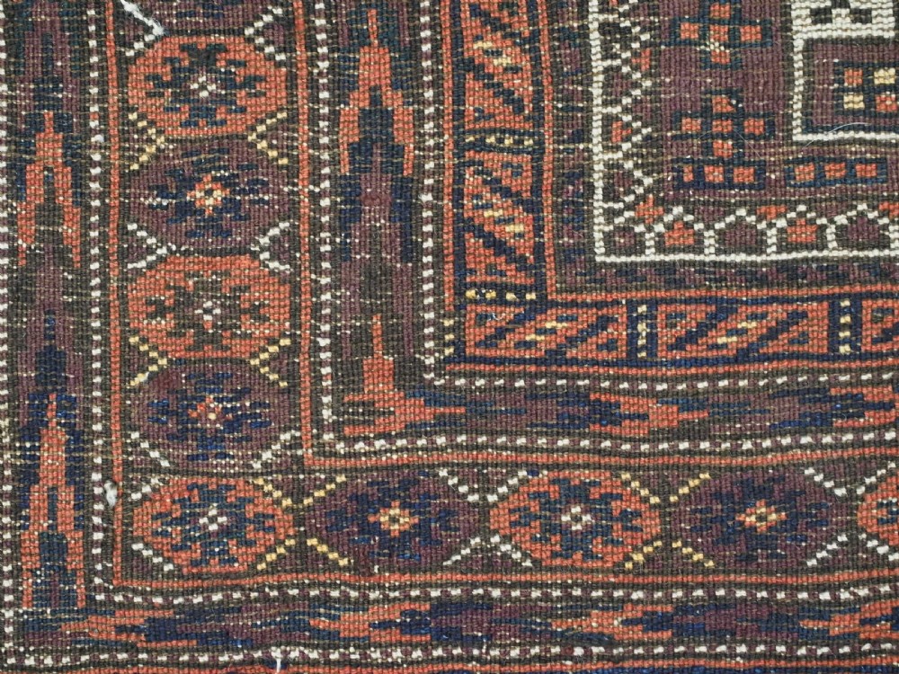 An antique hand-knotted wool Baluch rug featuring four octagonal central medallions on a deep aubergine ground with geometric borders. View XIV