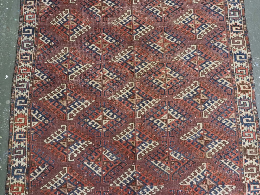 A hand-knotted antique Yomut Turkmen wool rug featuring repeating diamond-shaped geometric guls in red, navy, brown, and cream with patterned borders. View IV