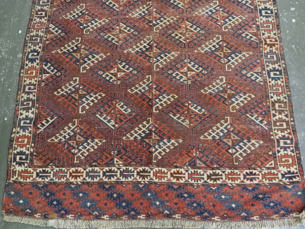 A hand-knotted antique Yomut Turkmen wool rug featuring repeating diamond-shaped geometric guls in red, navy, brown, and cream with patterned borders. View V