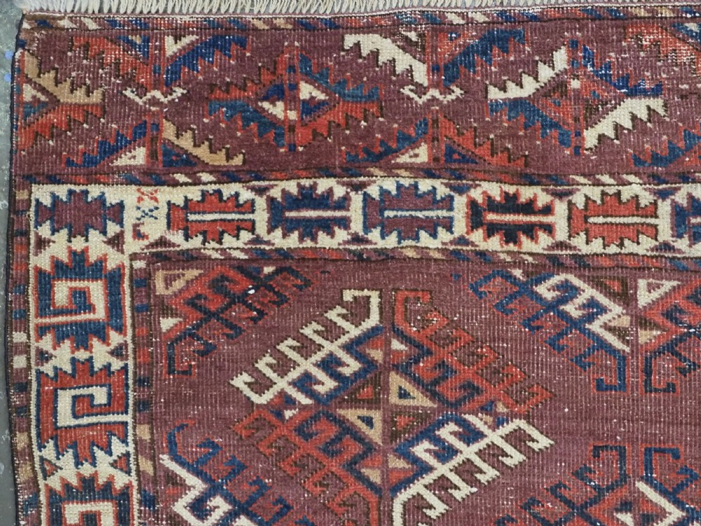 A hand-knotted antique Yomut Turkmen wool rug featuring repeating diamond-shaped geometric guls in red, navy, brown, and cream with patterned borders. View VI