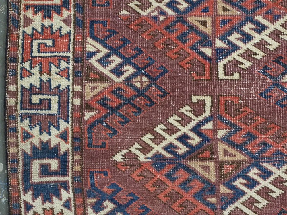 A hand-knotted antique Yomut Turkmen wool rug featuring repeating diamond-shaped geometric guls in red, navy, brown, and cream with patterned borders. View VII