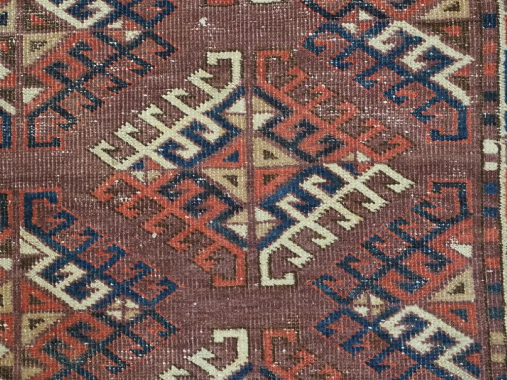 A hand-knotted antique Yomut Turkmen wool rug featuring repeating diamond-shaped geometric guls in red, navy, brown, and cream with patterned borders. View IX