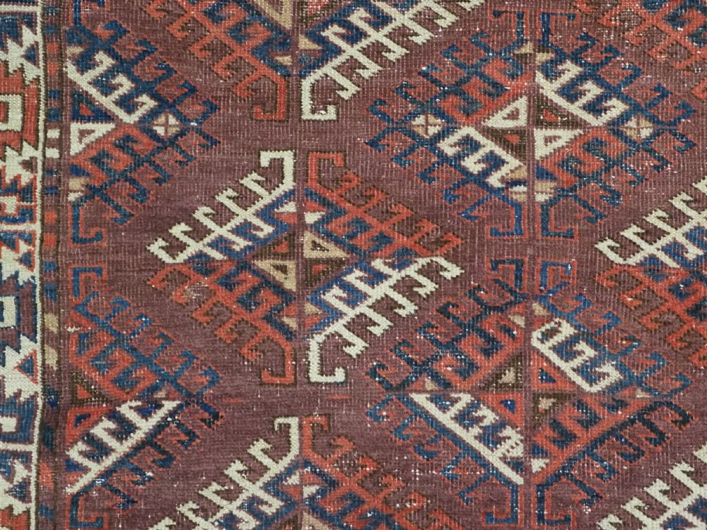 A hand-knotted antique Yomut Turkmen wool rug featuring repeating diamond-shaped geometric guls in red, navy, brown, and cream with patterned borders. View X
