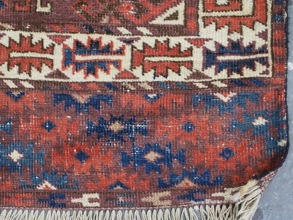 A hand-knotted antique Yomut Turkmen wool rug featuring repeating diamond-shaped geometric guls in red, navy, brown, and cream with patterned borders. View XII