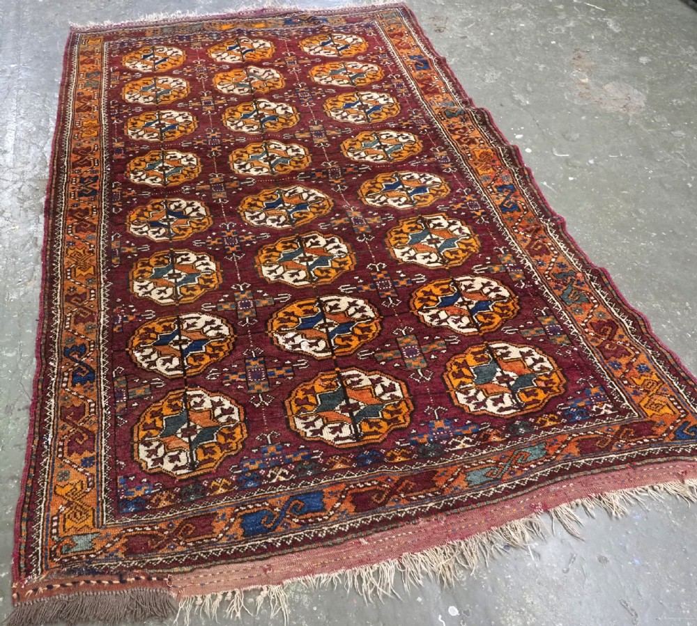 An antique hand-knotted Quchan Kurd rug featuring repeating cream and mustard octagonal Turkmen gul motifs set against a deep red field with geometric borders. View II