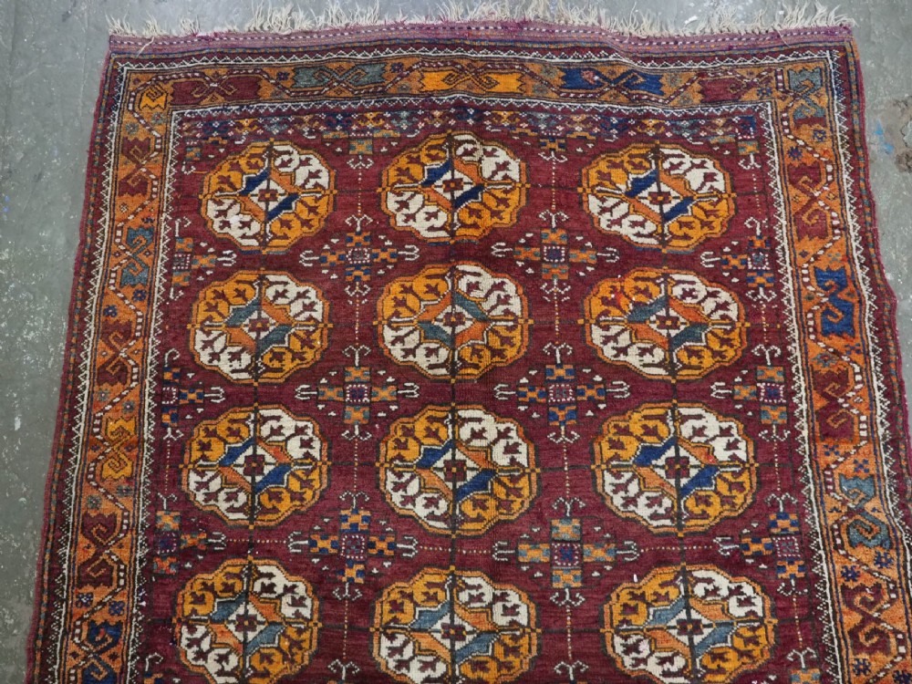 An antique hand-knotted Quchan Kurd rug featuring repeating cream and mustard octagonal Turkmen gul motifs set against a deep red field with geometric borders. View III