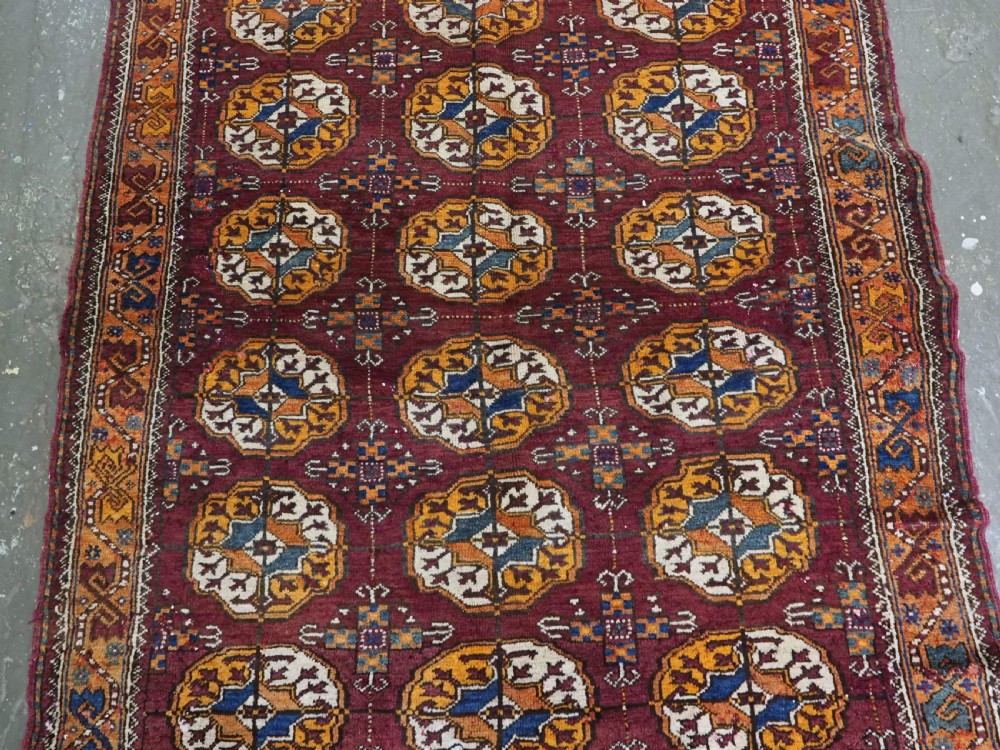An antique hand-knotted Quchan Kurd rug featuring repeating cream and mustard octagonal Turkmen gul motifs set against a deep red field with geometric borders. View IV