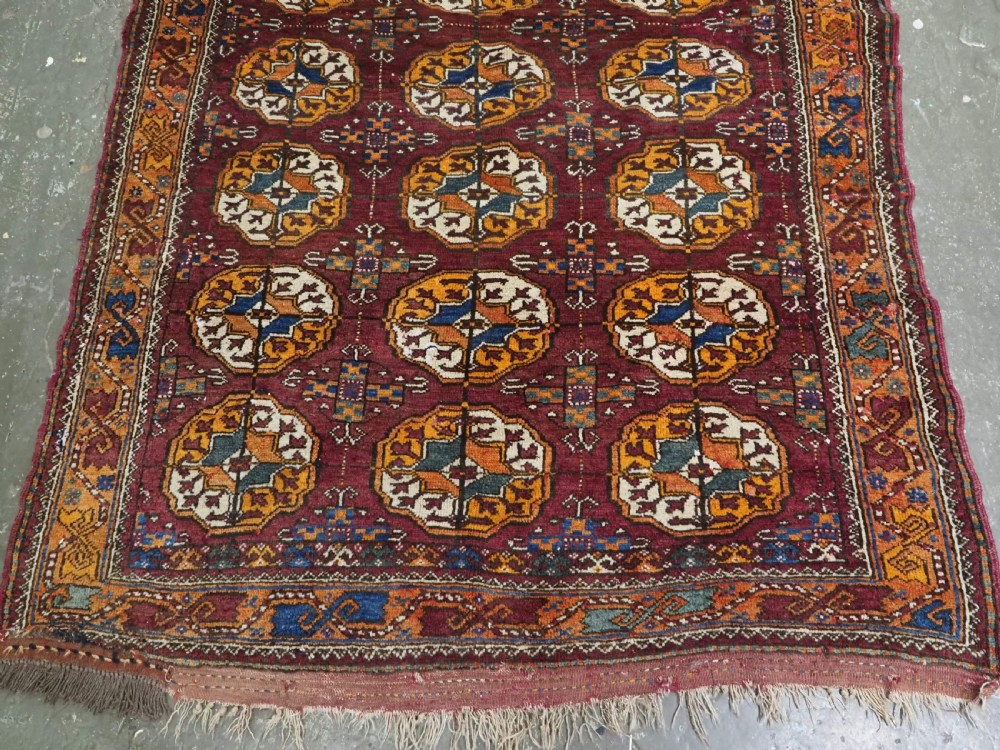 An antique hand-knotted Quchan Kurd rug featuring repeating cream and mustard octagonal Turkmen gul motifs set against a deep red field with geometric borders. View V