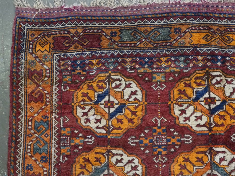 An antique hand-knotted Quchan Kurd rug featuring repeating cream and mustard octagonal Turkmen gul motifs set against a deep red field with geometric borders. View VI