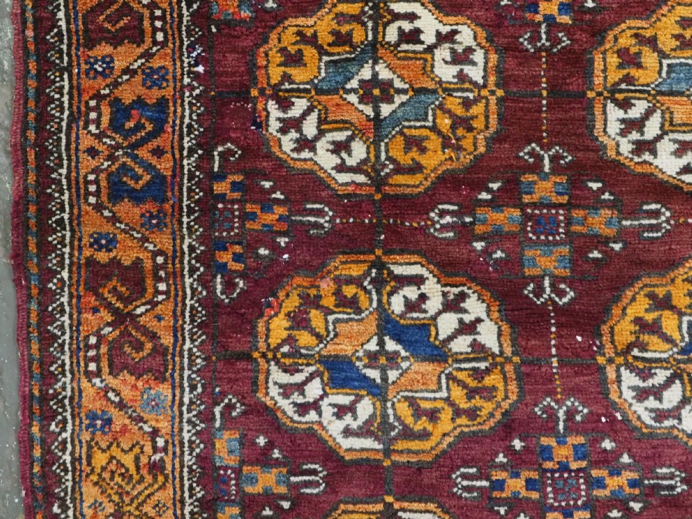 An antique hand-knotted Quchan Kurd rug featuring repeating cream and mustard octagonal Turkmen gul motifs set against a deep red field with geometric borders. View VII