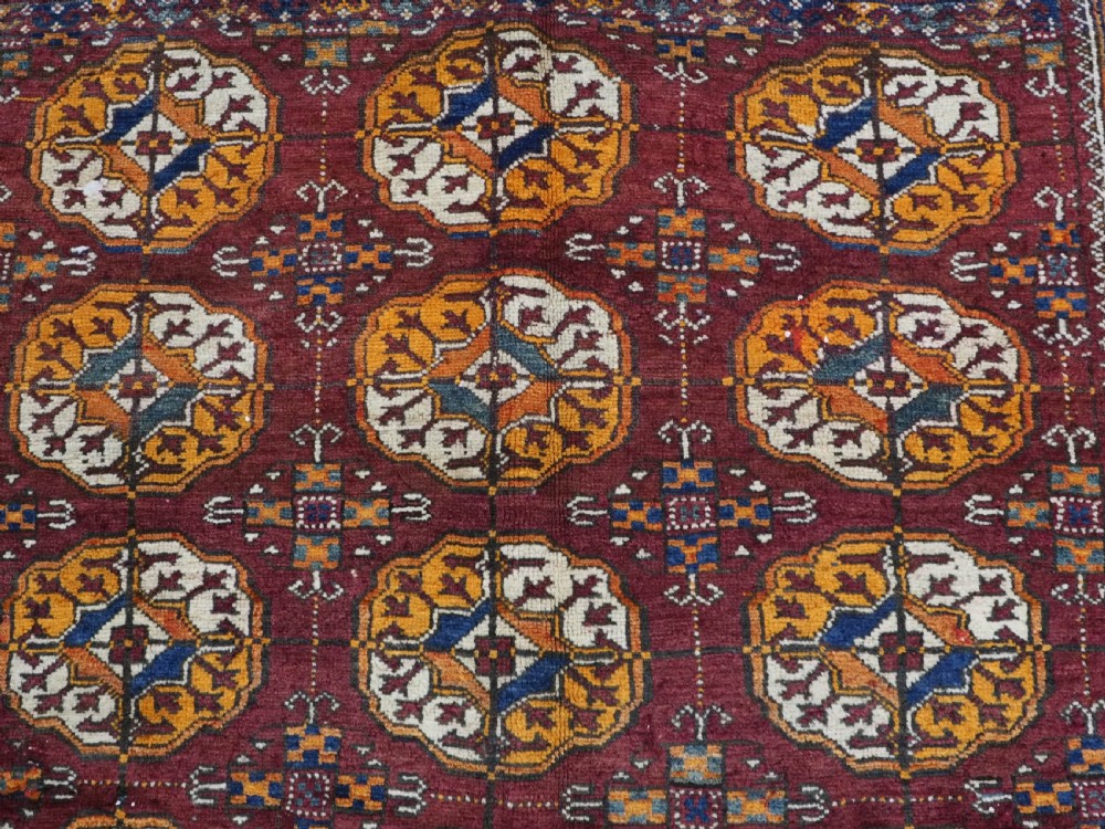 An antique hand-knotted Quchan Kurd rug featuring repeating cream and mustard octagonal Turkmen gul motifs set against a deep red field with geometric borders. View VIII