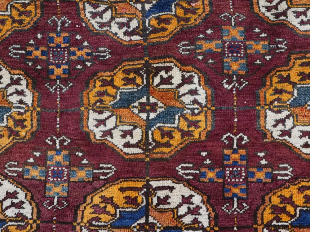 An antique hand-knotted Quchan Kurd rug featuring repeating cream and mustard octagonal Turkmen gul motifs set against a deep red field with geometric borders. View IX