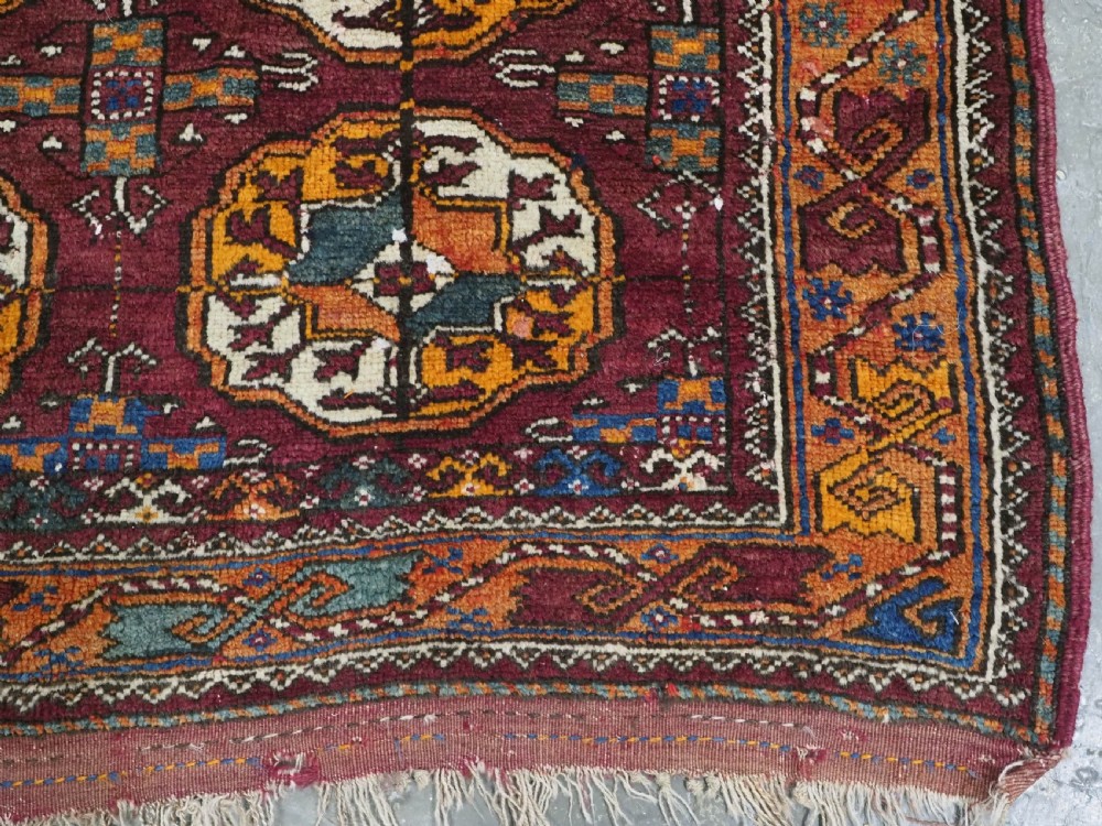 An antique hand-knotted Quchan Kurd rug featuring repeating cream and mustard octagonal Turkmen gul motifs set against a deep red field with geometric borders. View X