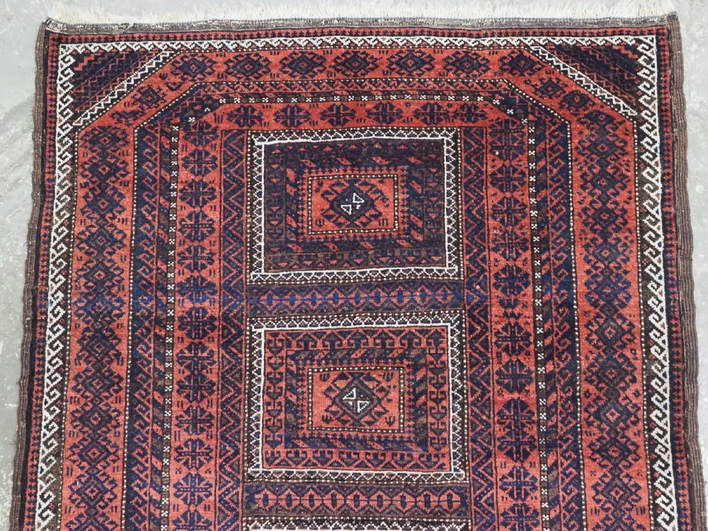 An antique Baluch hand-knotted wool rug featuring five geometric square medallions along a central field in deep red, dark navy blue, and terracotta tones. View III